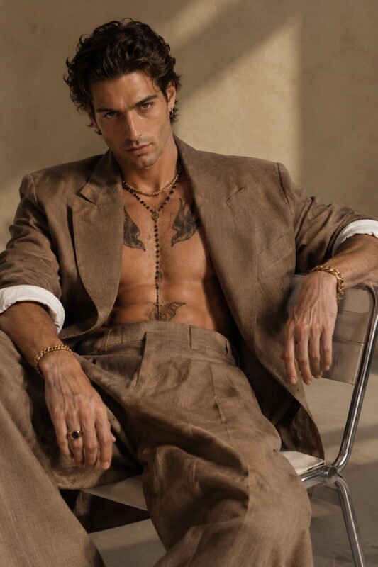 Homme au style dandy moderne portant un collier et un bracelet en maille dorée avec une veste élégante.