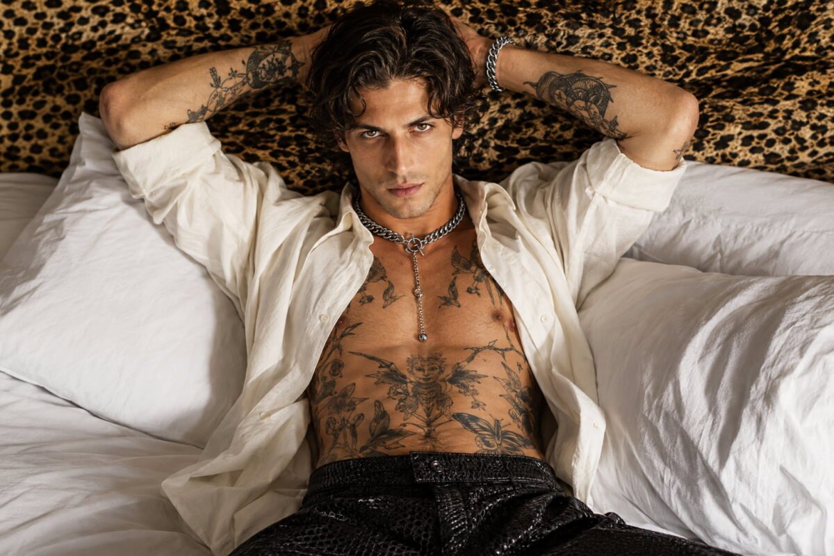 Homme au style glam rock chic portant des bijoux en maille métallique avec une tenue noire élégante.